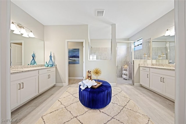 full bath with visible vents, a shower stall, wood finish floors, baseboards, and two vanities