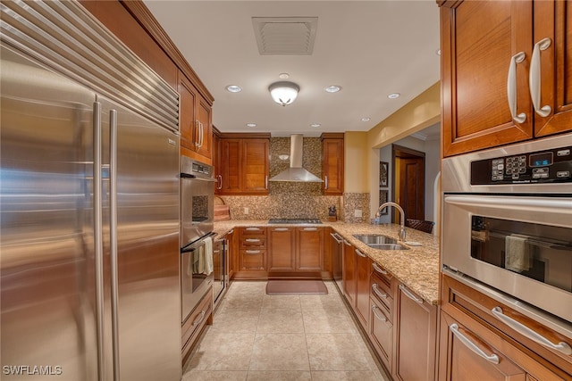 kitchen with tasteful backsplash, light stone counters, wall chimney exhaust hood, stainless steel appliances, and sink