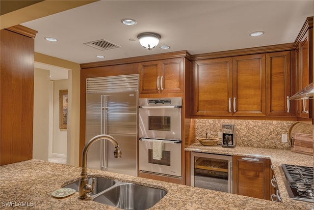 kitchen with appliances with stainless steel finishes, light stone countertops, wine cooler, tasteful backsplash, and sink