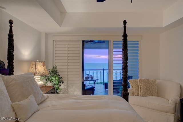 tiled bedroom with a tray ceiling, a water view, and access to exterior