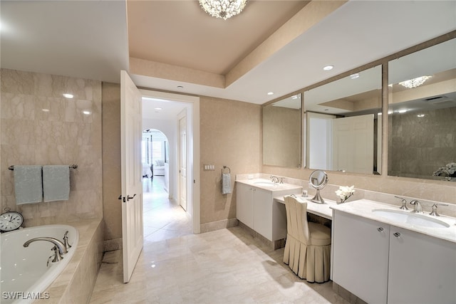 bathroom featuring a tray ceiling, tiled bath, vanity, and tile patterned flooring