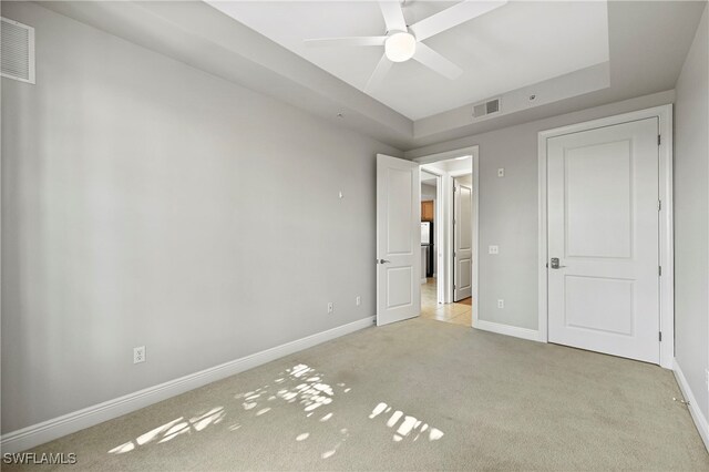 unfurnished bedroom featuring ceiling fan, a raised ceiling, and light colored carpet