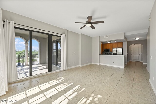 unfurnished living room with light tile patterned floors, visible vents, arched walkways, baseboards, and a ceiling fan