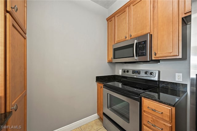 kitchen featuring light tile patterned floors, appliances with stainless steel finishes, and dark stone counters