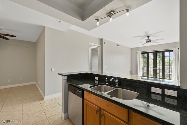 kitchen with light tile patterned floors, brown cabinetry, dishwasher, dark stone countertops, and a sink