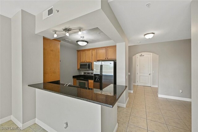 kitchen with appliances with stainless steel finishes, kitchen peninsula, track lighting, and light tile patterned floors