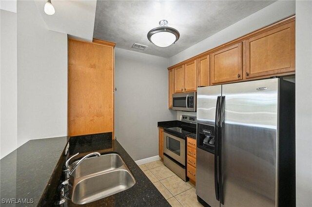 kitchen with appliances with stainless steel finishes, light tile patterned flooring, sink, and dark stone counters