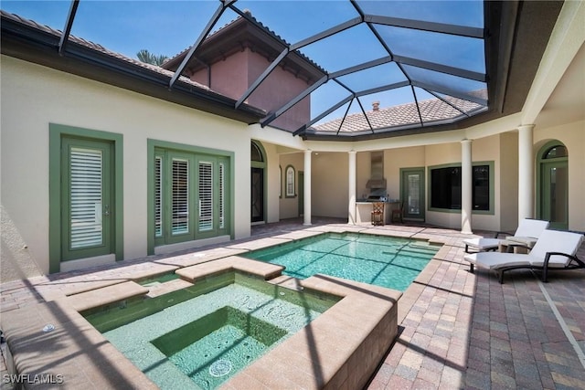 view of pool featuring glass enclosure, an in ground hot tub, a patio area, and an outdoor kitchen