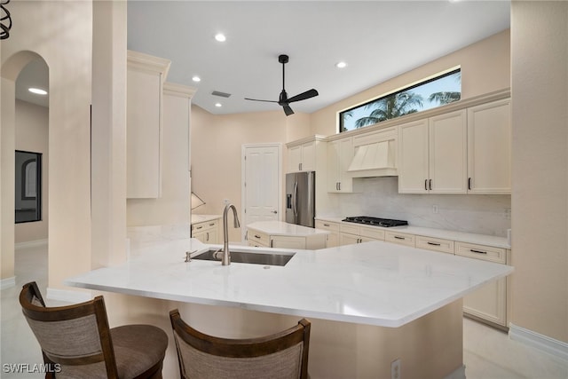 kitchen with sink, a kitchen breakfast bar, stainless steel refrigerator with ice dispenser, custom exhaust hood, and kitchen peninsula