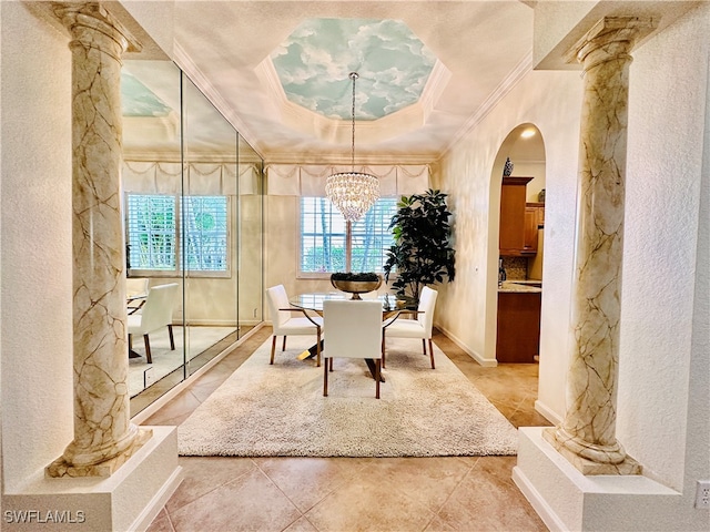 tiled dining area featuring ornate columns, an inviting chandelier, crown molding, and a raised ceiling