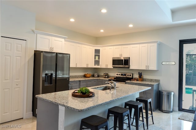 kitchen featuring white cabinetry, stainless steel appliances, sink, light stone countertops, and a kitchen island with sink