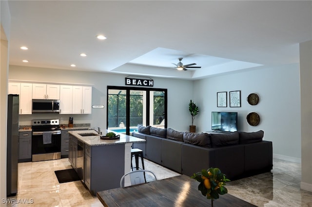 kitchen with appliances with stainless steel finishes, an island with sink, white cabinetry, ceiling fan, and a raised ceiling