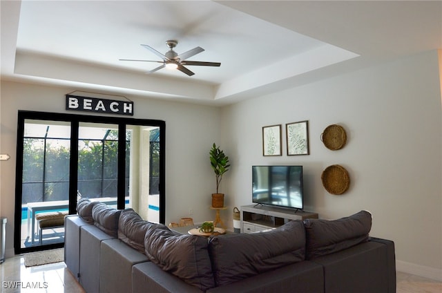 living room with a raised ceiling, light tile patterned floors, and ceiling fan