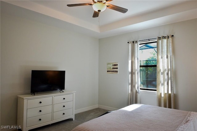 bedroom featuring a raised ceiling, ceiling fan, and dark colored carpet