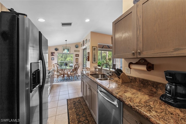 kitchen with dark stone countertops, light tile patterned floors, decorative light fixtures, stainless steel appliances, and sink