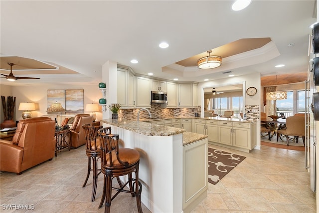 kitchen with light stone counters, kitchen peninsula, ceiling fan, a breakfast bar, and a tray ceiling