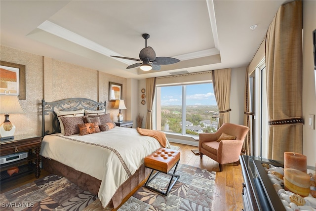 bedroom with ceiling fan, light wood-type flooring, and a tray ceiling