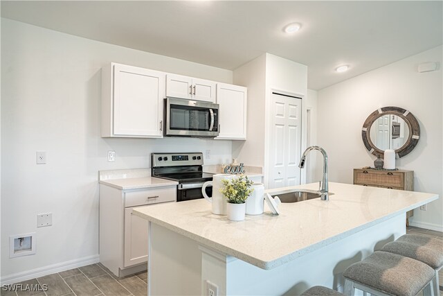 kitchen with stainless steel appliances, sink, light stone counters, a kitchen island with sink, and a breakfast bar