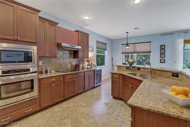 kitchen with stainless steel appliances, sink, light stone counters, hanging light fixtures, and wine cooler