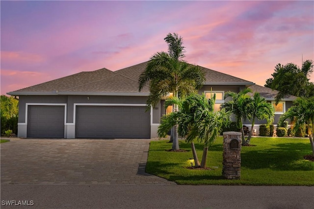 view of front facade with decorative driveway, a lawn, an attached garage, and stucco siding