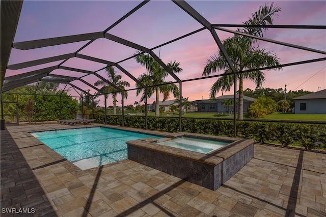 pool at dusk with an in ground hot tub, a lanai, and a patio