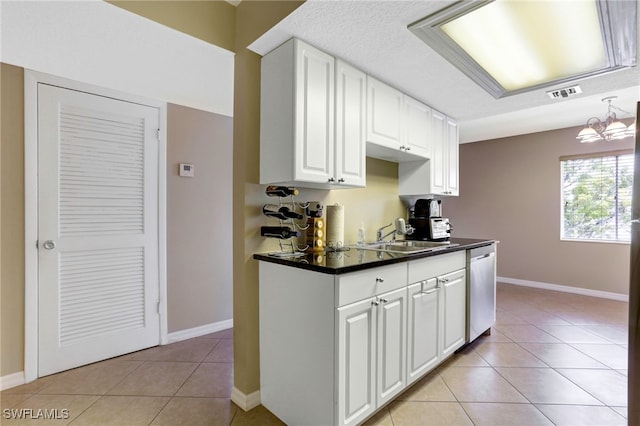 kitchen with white cabinetry, sink, stainless steel dishwasher, light tile patterned floors, and an inviting chandelier