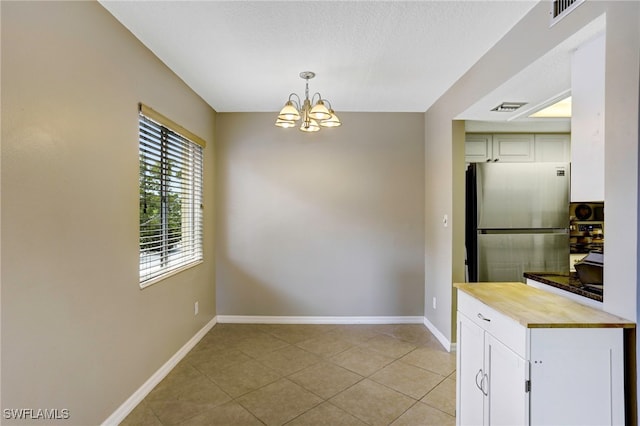 unfurnished dining area with light tile patterned floors, a notable chandelier, and a textured ceiling