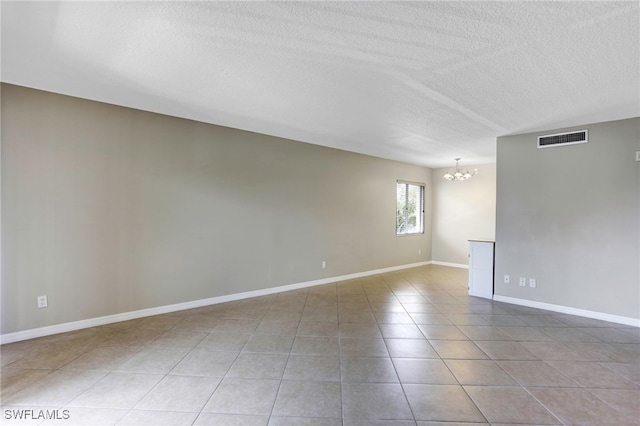 tiled empty room featuring a textured ceiling and an inviting chandelier