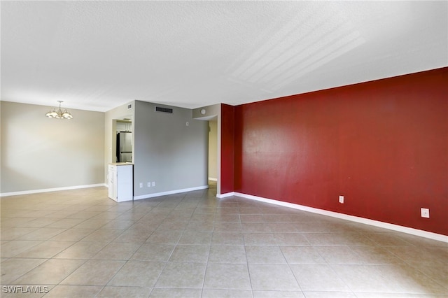 empty room with tile patterned flooring, a textured ceiling, and a notable chandelier