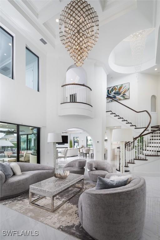 living room featuring an inviting chandelier, a high ceiling, coffered ceiling, ornamental molding, and beamed ceiling