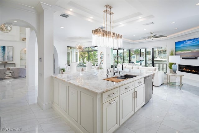 kitchen featuring pendant lighting, sink, crown molding, light stone countertops, and a center island with sink