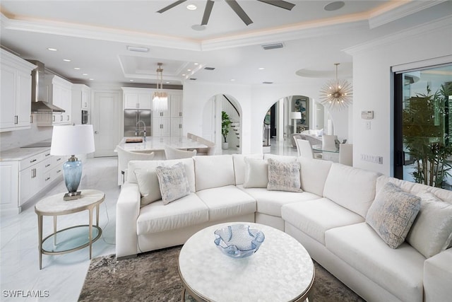 living room with crown molding, sink, a tray ceiling, and ceiling fan with notable chandelier