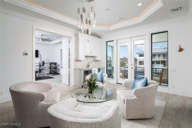 living room featuring french doors, a tray ceiling, light wood-type flooring, and crown molding