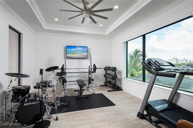 exercise room with ceiling fan, ornamental molding, a tray ceiling, and light hardwood / wood-style flooring