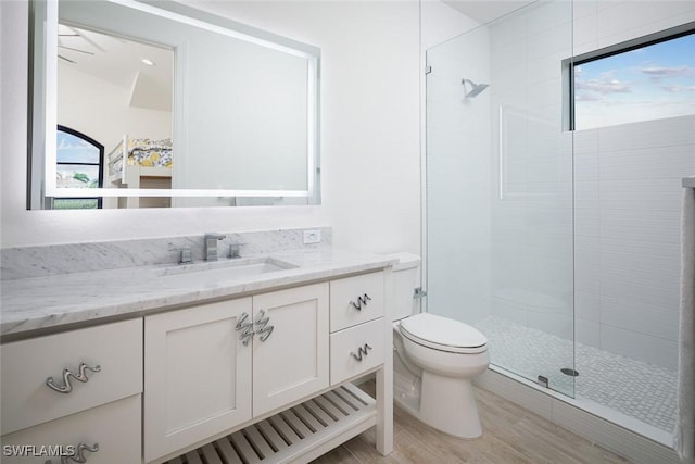 bathroom with hardwood / wood-style floors, vanity, a tile shower, and toilet