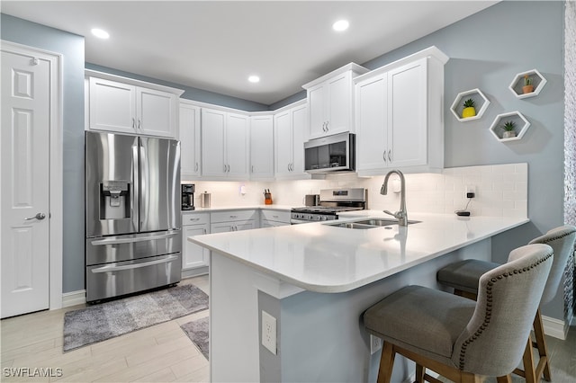 kitchen featuring tasteful backsplash, kitchen peninsula, white cabinets, appliances with stainless steel finishes, and sink