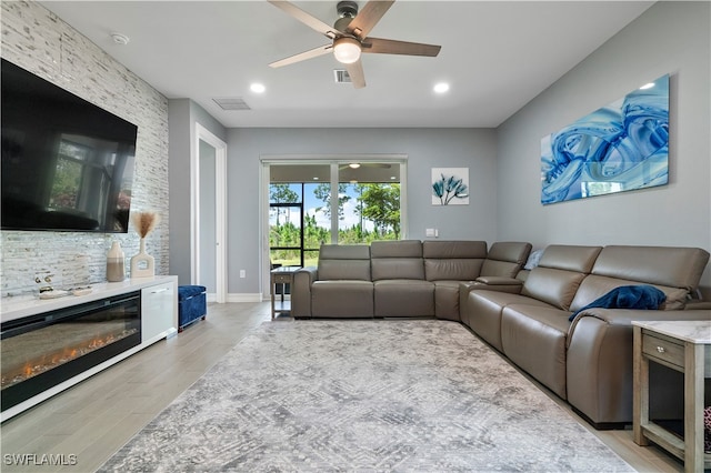 living room featuring a stone fireplace, ceiling fan, and light wood-type flooring