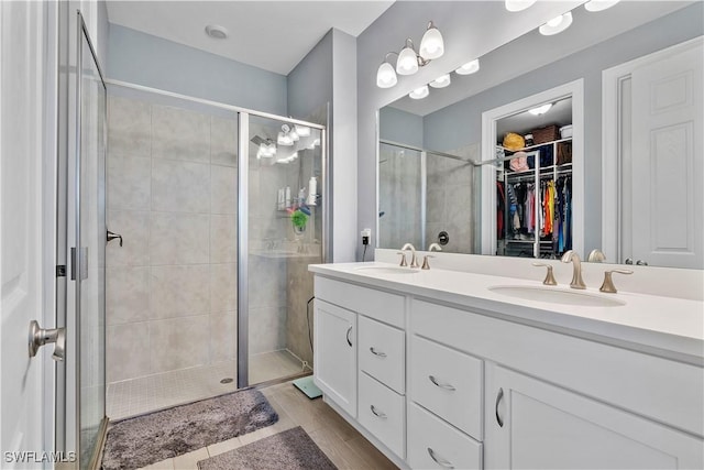 full bath with double vanity, a stall shower, a walk in closet, and a sink