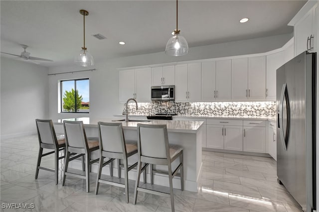 kitchen with appliances with stainless steel finishes, pendant lighting, white cabinets, decorative backsplash, and a center island with sink