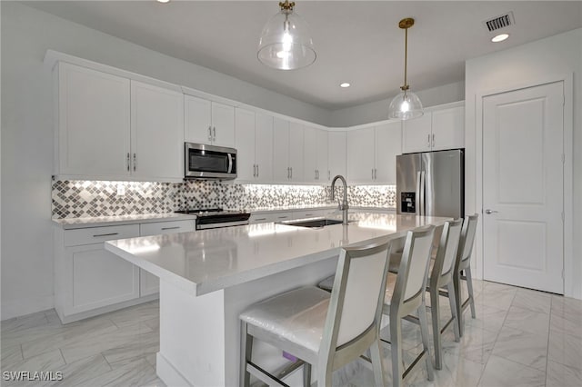 kitchen with white cabinetry, appliances with stainless steel finishes, sink, and a center island with sink