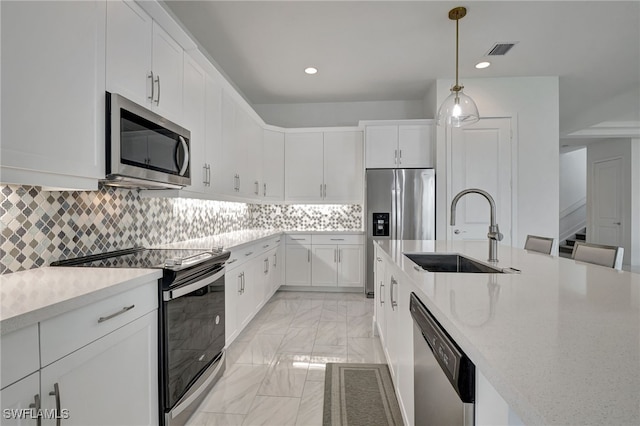 kitchen featuring appliances with stainless steel finishes, tasteful backsplash, white cabinetry, sink, and hanging light fixtures