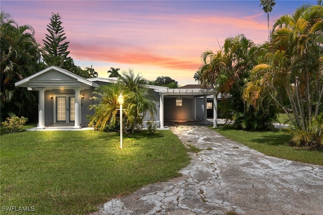 view of front of house with stucco siding, driveway, a front lawn, french doors, and an attached carport