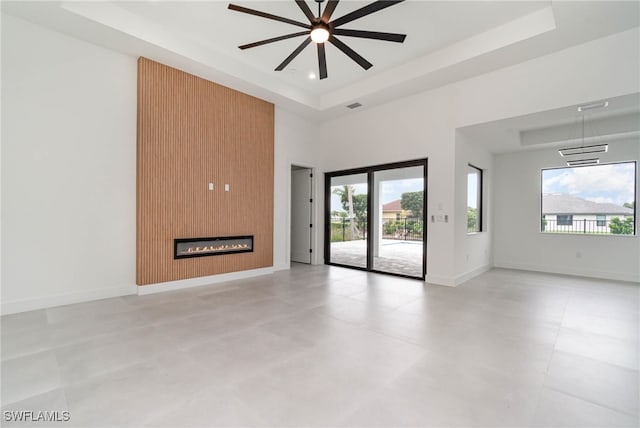 unfurnished living room featuring ceiling fan, a fireplace, light tile patterned floors, and a tray ceiling