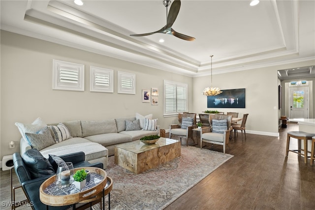 living room with dark hardwood / wood-style flooring, ceiling fan with notable chandelier, a raised ceiling, and crown molding