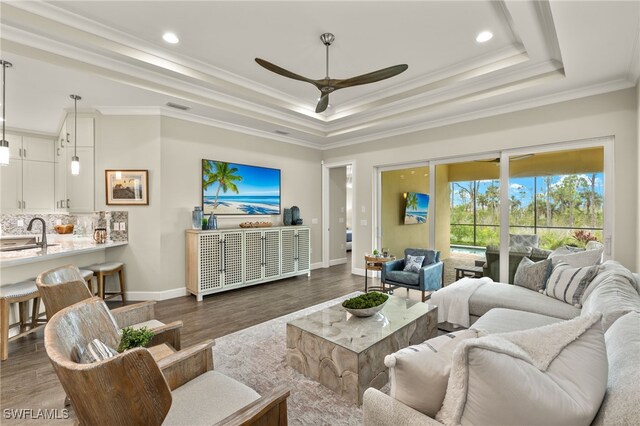 living room featuring a raised ceiling, sink, dark hardwood / wood-style floors, ceiling fan, and ornamental molding