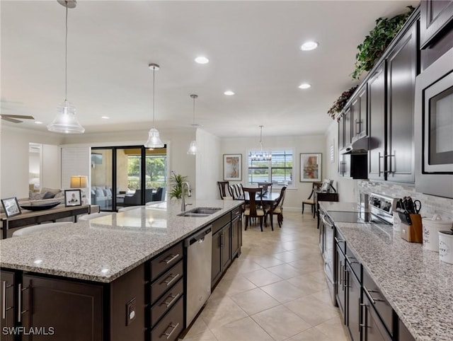 kitchen with sink, appliances with stainless steel finishes, hanging light fixtures, light stone counters, and an island with sink