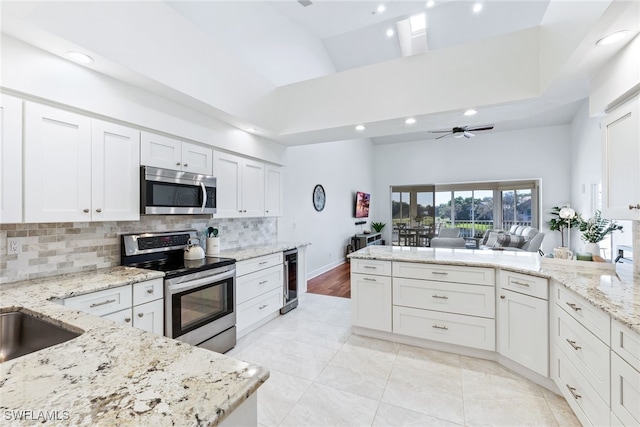 kitchen featuring stainless steel appliances, wine cooler, a high ceiling, a peninsula, and decorative backsplash