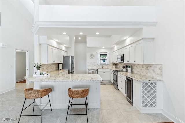 kitchen featuring beverage cooler, light stone countertops, a peninsula, stainless steel appliances, and a kitchen breakfast bar