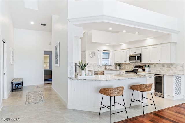 kitchen featuring beverage cooler, a kitchen bar, light stone counters, a peninsula, and stainless steel appliances