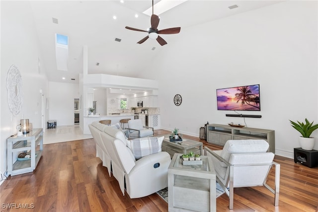 living area with wood finished floors, baseboards, a skylight, ceiling fan, and a towering ceiling